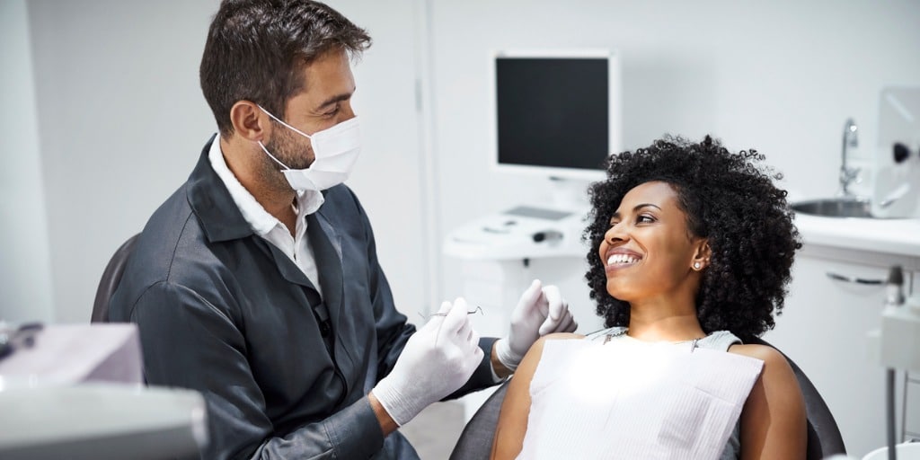 dentist examining smiling female patient in clinic